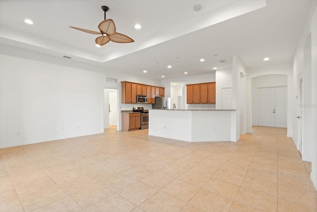 kitchen with light tile patterned floors, stainless steel appliances, ceiling fan, and a tray ceiling