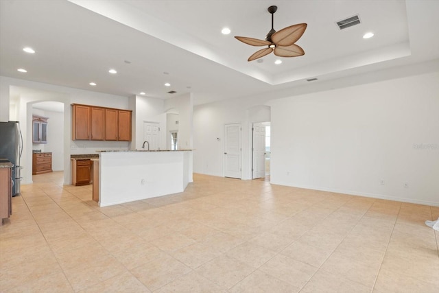 kitchen with ceiling fan, stainless steel fridge, a raised ceiling, and a kitchen island