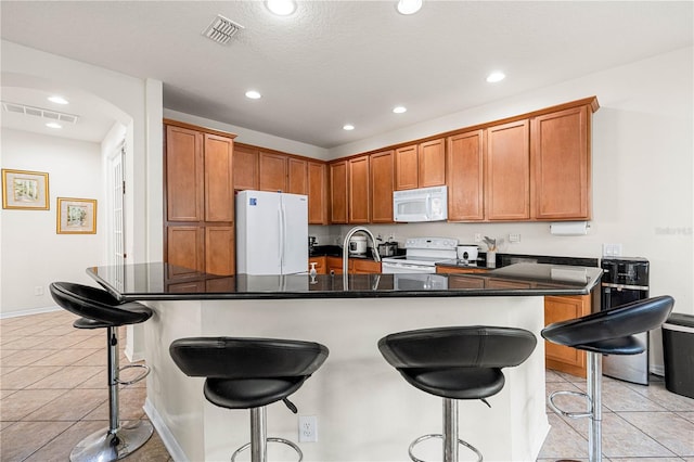 kitchen with a breakfast bar, a center island with sink, light tile patterned floors, and white appliances