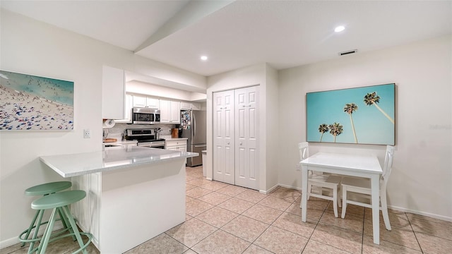 kitchen featuring white cabinetry, kitchen peninsula, a breakfast bar, light tile patterned flooring, and appliances with stainless steel finishes