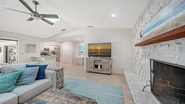 tiled living room featuring vaulted ceiling, ceiling fan, and a stone fireplace