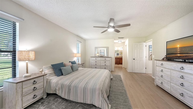 bedroom with ensuite bathroom, light hardwood / wood-style flooring, ceiling fan, and a textured ceiling