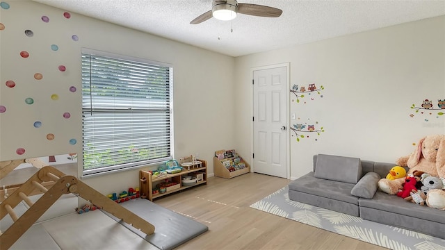 rec room with ceiling fan, light hardwood / wood-style floors, and a textured ceiling