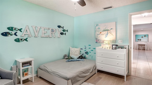 bedroom with ceiling fan, light hardwood / wood-style flooring, and a textured ceiling