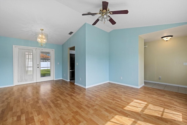 unfurnished living room featuring ceiling fan with notable chandelier, light wood-type flooring, french doors, and vaulted ceiling