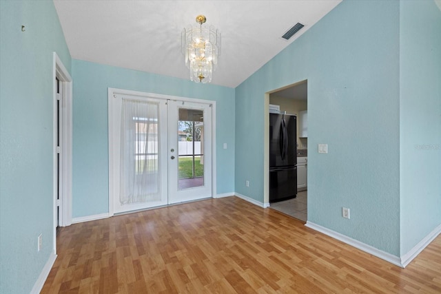 spare room with a chandelier, french doors, light hardwood / wood-style floors, and lofted ceiling