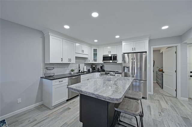 kitchen featuring sink, light hardwood / wood-style floors, dark stone counters, white cabinets, and appliances with stainless steel finishes