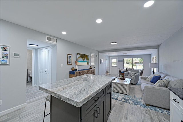 kitchen featuring a kitchen bar, light stone counters, a center island, and light hardwood / wood-style floors