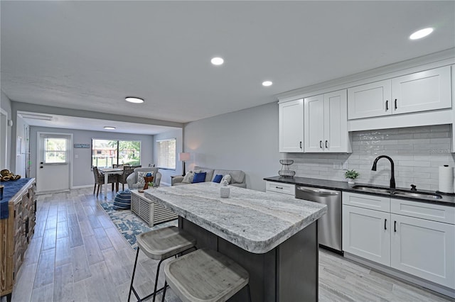 kitchen with decorative backsplash, light wood-type flooring, stainless steel dishwasher, sink, and white cabinets