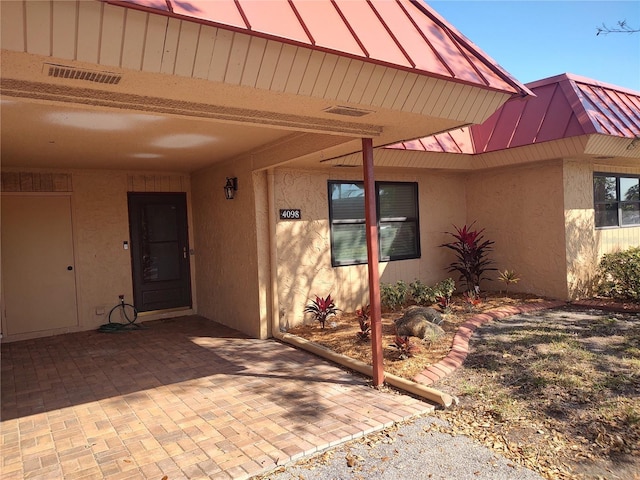 property entrance featuring a standing seam roof, visible vents, metal roof, and stucco siding