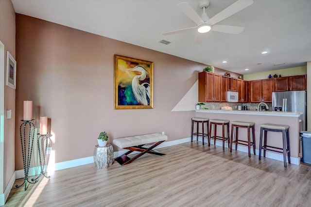 kitchen featuring kitchen peninsula, a kitchen bar, tasteful backsplash, ceiling fan, and light hardwood / wood-style flooring