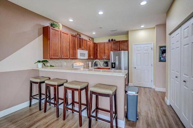 kitchen featuring tasteful backsplash, kitchen peninsula, white appliances, a kitchen bar, and light wood-type flooring