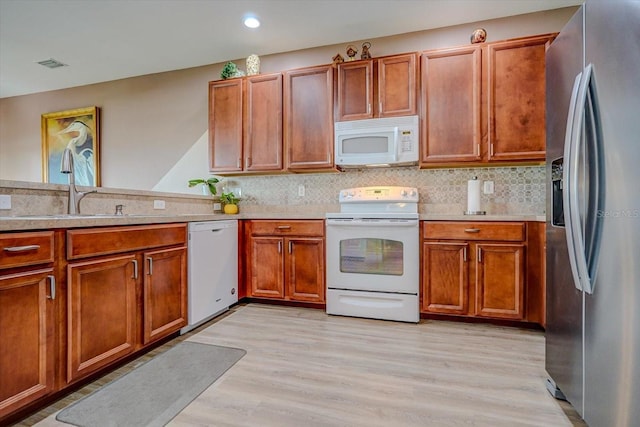 kitchen with kitchen peninsula, light wood-type flooring, tasteful backsplash, white appliances, and sink