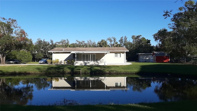 back of property featuring a lawn, a water view, and a shed