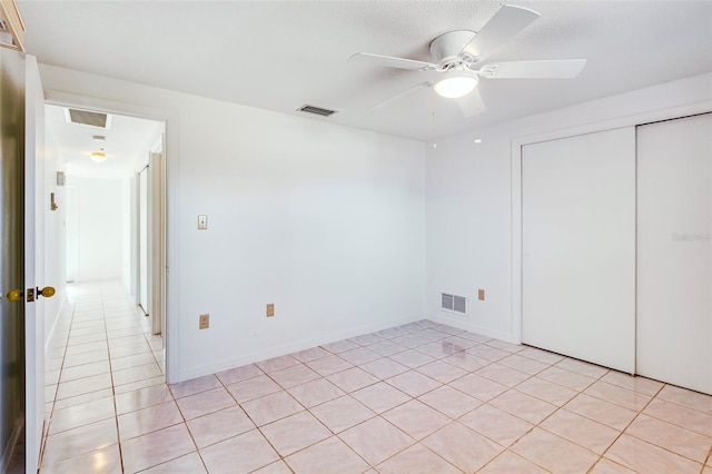 unfurnished bedroom with ceiling fan, light tile patterned floors, a textured ceiling, and a closet