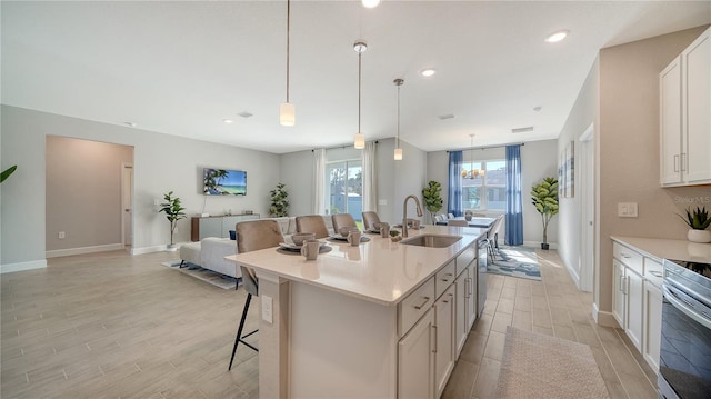 kitchen with a kitchen breakfast bar, a kitchen island with sink, sink, white cabinetry, and hanging light fixtures