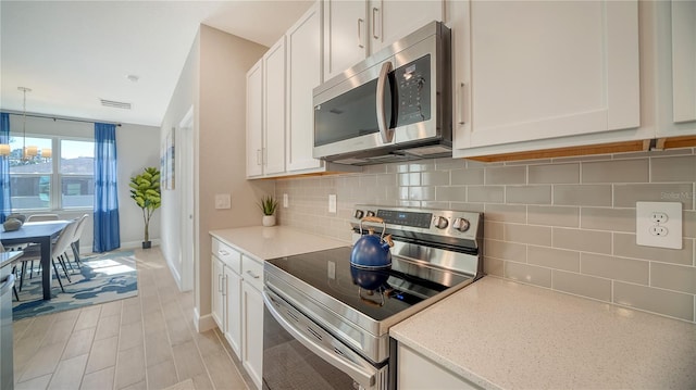 kitchen featuring decorative light fixtures, decorative backsplash, white cabinetry, and appliances with stainless steel finishes