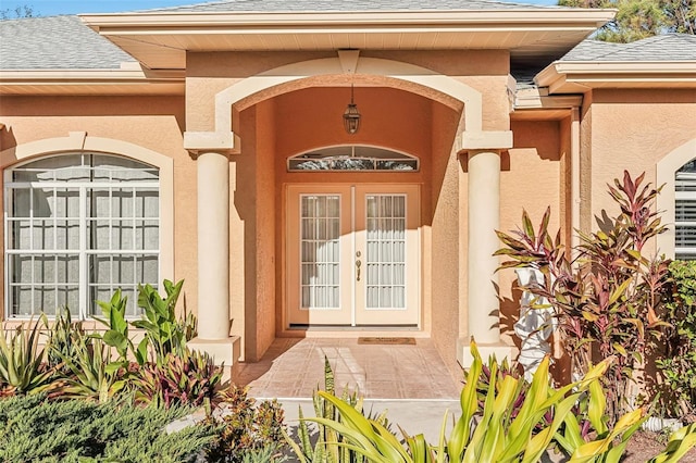property entrance with a shingled roof, stucco siding, and french doors