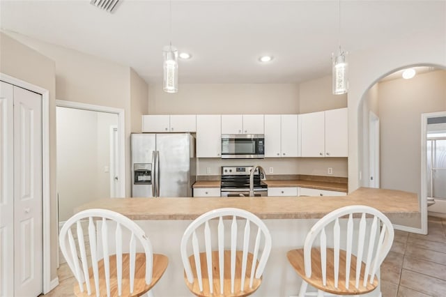 kitchen featuring appliances with stainless steel finishes, a kitchen bar, light countertops, white cabinetry, and decorative light fixtures