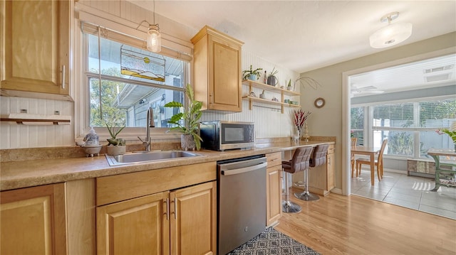 kitchen with pendant lighting, light brown cabinets, sink, light wood-type flooring, and appliances with stainless steel finishes