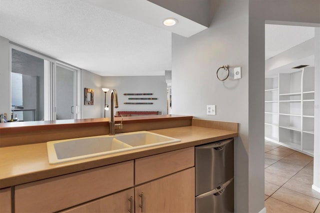 kitchen with light tile patterned floors, a textured ceiling, stainless steel dishwasher, and sink