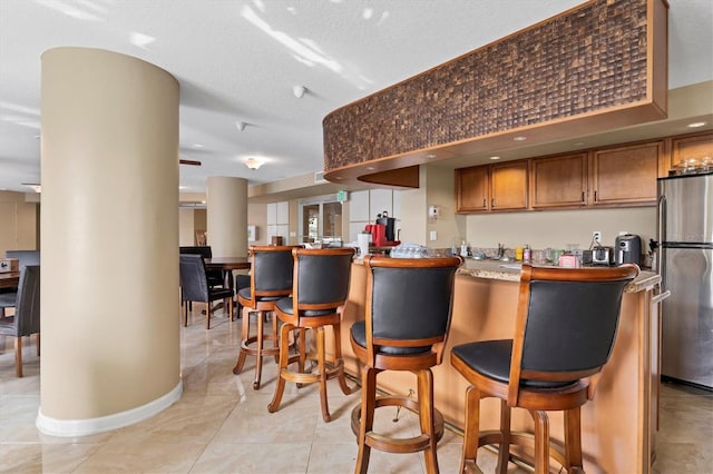 bar featuring stainless steel fridge, a textured ceiling, and light tile patterned floors