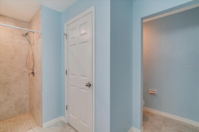 bathroom with toilet, tile patterned flooring, and a tile shower