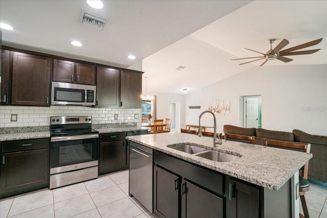 kitchen with appliances with stainless steel finishes, lofted ceiling, an island with sink, decorative backsplash, and sink