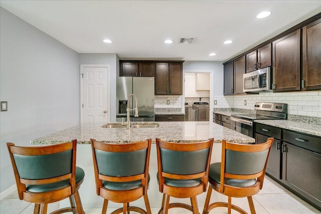 kitchen with washer and dryer, stainless steel appliances, and a center island with sink