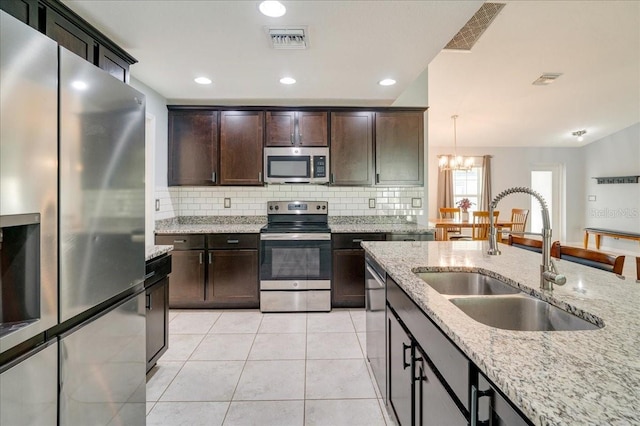 kitchen featuring pendant lighting, sink, appliances with stainless steel finishes, light stone counters, and a chandelier