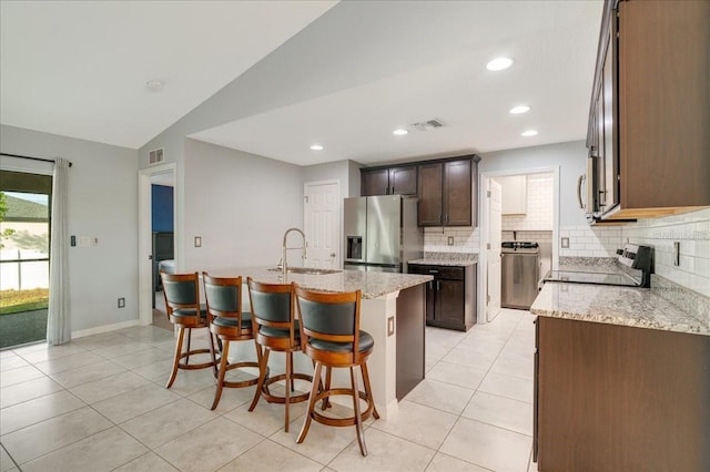 kitchen with appliances with stainless steel finishes, lofted ceiling, sink, light stone counters, and a center island with sink