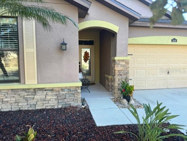 doorway to property featuring an attached garage, stone siding, and stucco siding