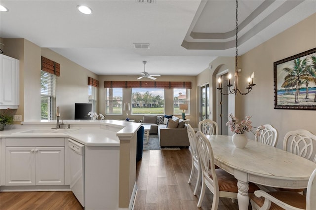 kitchen featuring white dishwasher, ceiling fan with notable chandelier, hanging light fixtures, light wood-type flooring, and white cabinetry