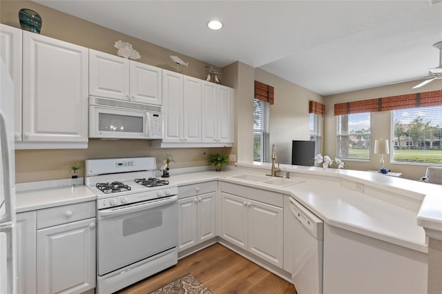 kitchen featuring kitchen peninsula, white appliances, sink, hardwood / wood-style flooring, and white cabinets