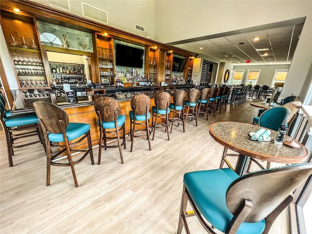 bar with a drop ceiling and light hardwood / wood-style flooring