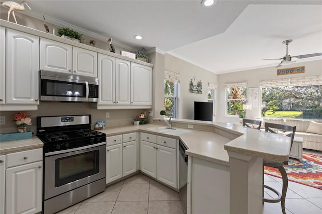 kitchen featuring kitchen peninsula, appliances with stainless steel finishes, ornamental molding, white cabinetry, and a breakfast bar area