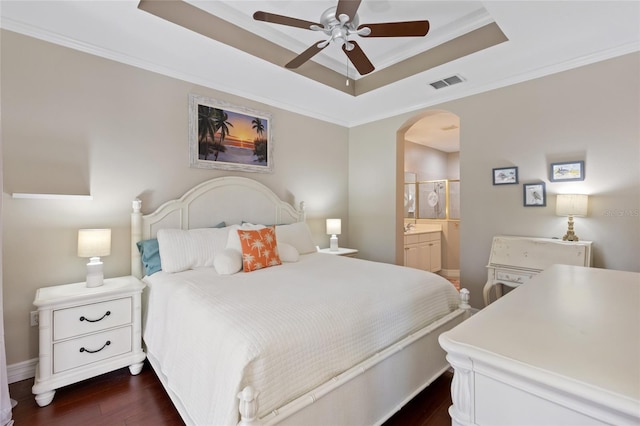 bedroom with dark wood-type flooring, ensuite bathroom, a raised ceiling, ceiling fan, and ornamental molding