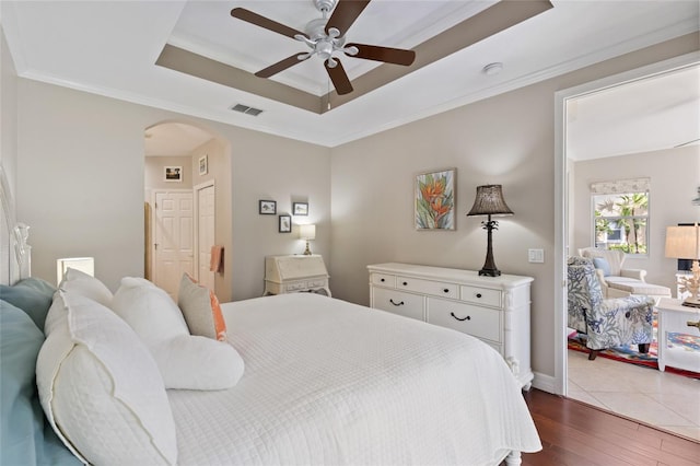 bedroom with a tray ceiling, ceiling fan, crown molding, hardwood / wood-style floors, and a closet