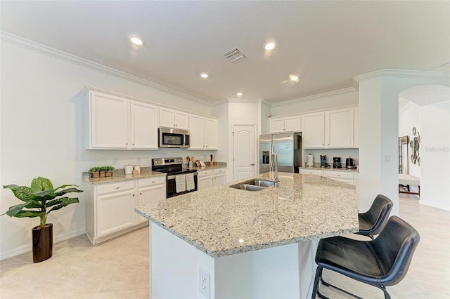 kitchen with light stone counters, stainless steel appliances, white cabinetry, and an island with sink