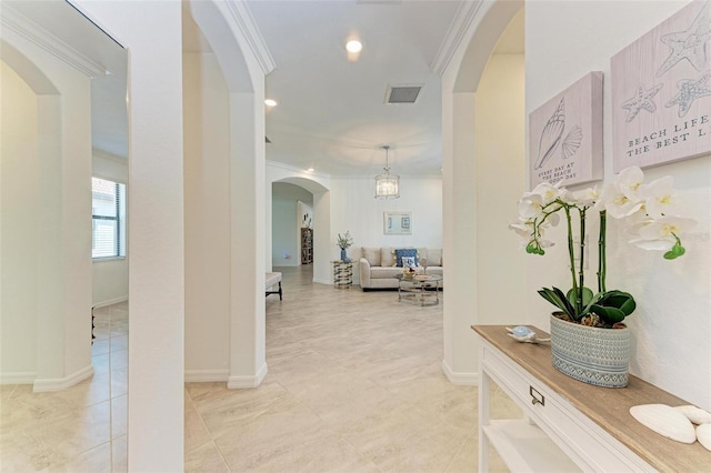 hallway with light tile patterned floors, an inviting chandelier, and crown molding