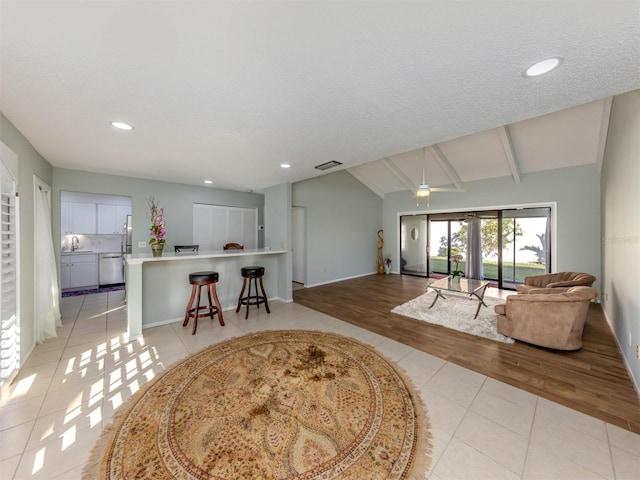 tiled living room with ceiling fan, sink, a textured ceiling, and lofted ceiling with beams