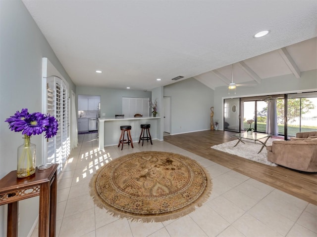 tiled living room with ceiling fan and vaulted ceiling with beams