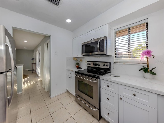 kitchen featuring white cabinetry, stainless steel appliances, tasteful backsplash, light tile patterned flooring, and light stone counters