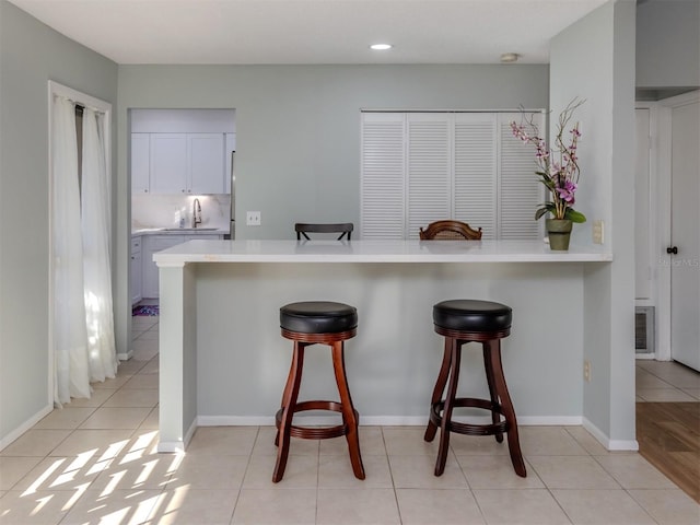 kitchen with white cabinetry, sink, kitchen peninsula, light tile patterned floors, and a breakfast bar area