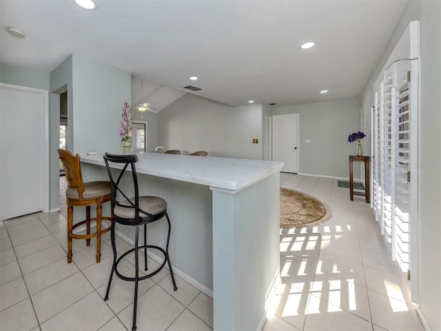 kitchen with a kitchen breakfast bar, light tile patterned flooring, and light stone countertops