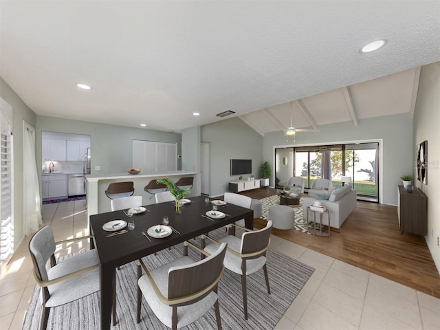 dining area featuring light tile patterned floors, ceiling fan, vaulted ceiling with beams, a textured ceiling, and sink