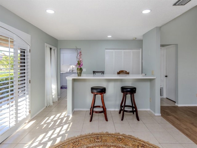 kitchen with light tile patterned flooring, white cabinetry, kitchen peninsula, and a breakfast bar