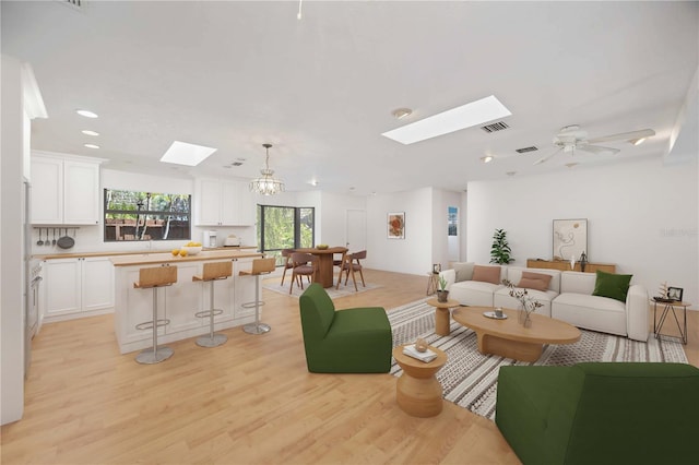 living room with light wood-type flooring, ceiling fan with notable chandelier, and a skylight