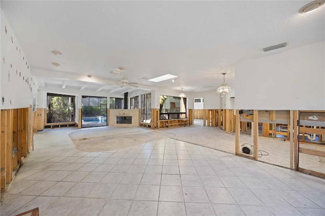 interior space with beamed ceiling, ceiling fan with notable chandelier, light tile patterned floors, and wooden walls