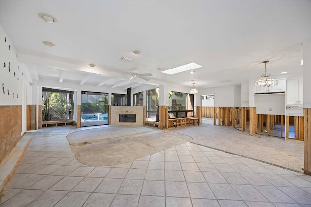 unfurnished living room with lofted ceiling with skylight, light tile patterned flooring, and ceiling fan with notable chandelier